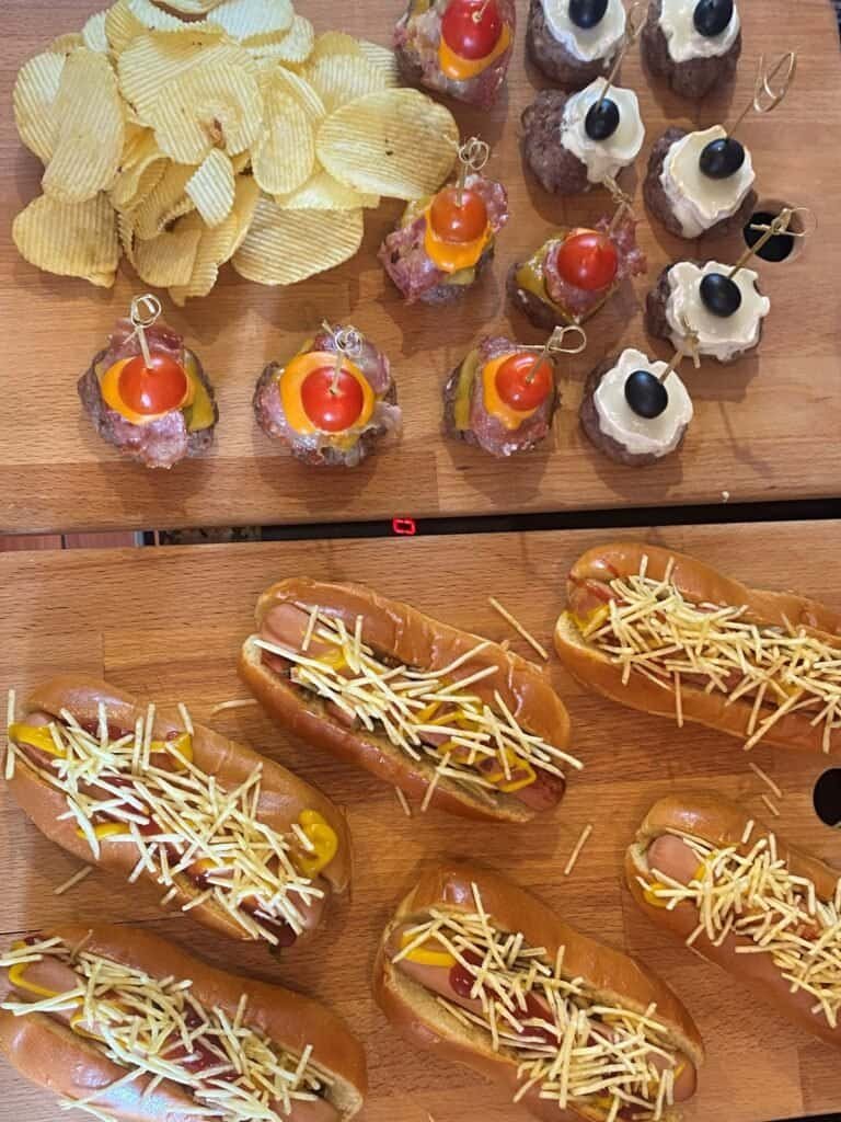 Mesa com serviço de catering gourmet a bordo, com petiscos como mini hambúrgueres, hot dogs artesanais, snacks e sobremesas em copo. Ideal para eventos privados ou passeios de barco com catering incluído em Lisboa, proporcionando uma experiência gastronómica única no rio Tejo.