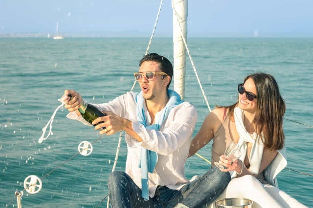 Jovem casal apaixonado num barco à vela a brindar com uma garrafa de champanhe - Festa de aniversário da namorada feliz num cruzeiro num veleiro de luxo