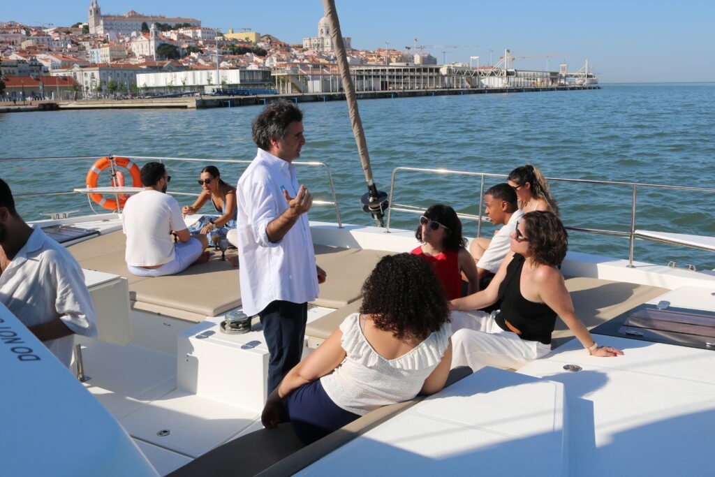 Concierges de prestigiosos hoteles de Lisboa compartiendo experiencias mientras navegaban por el Tajo, con el icónico paisaje de la ciudad de fondo